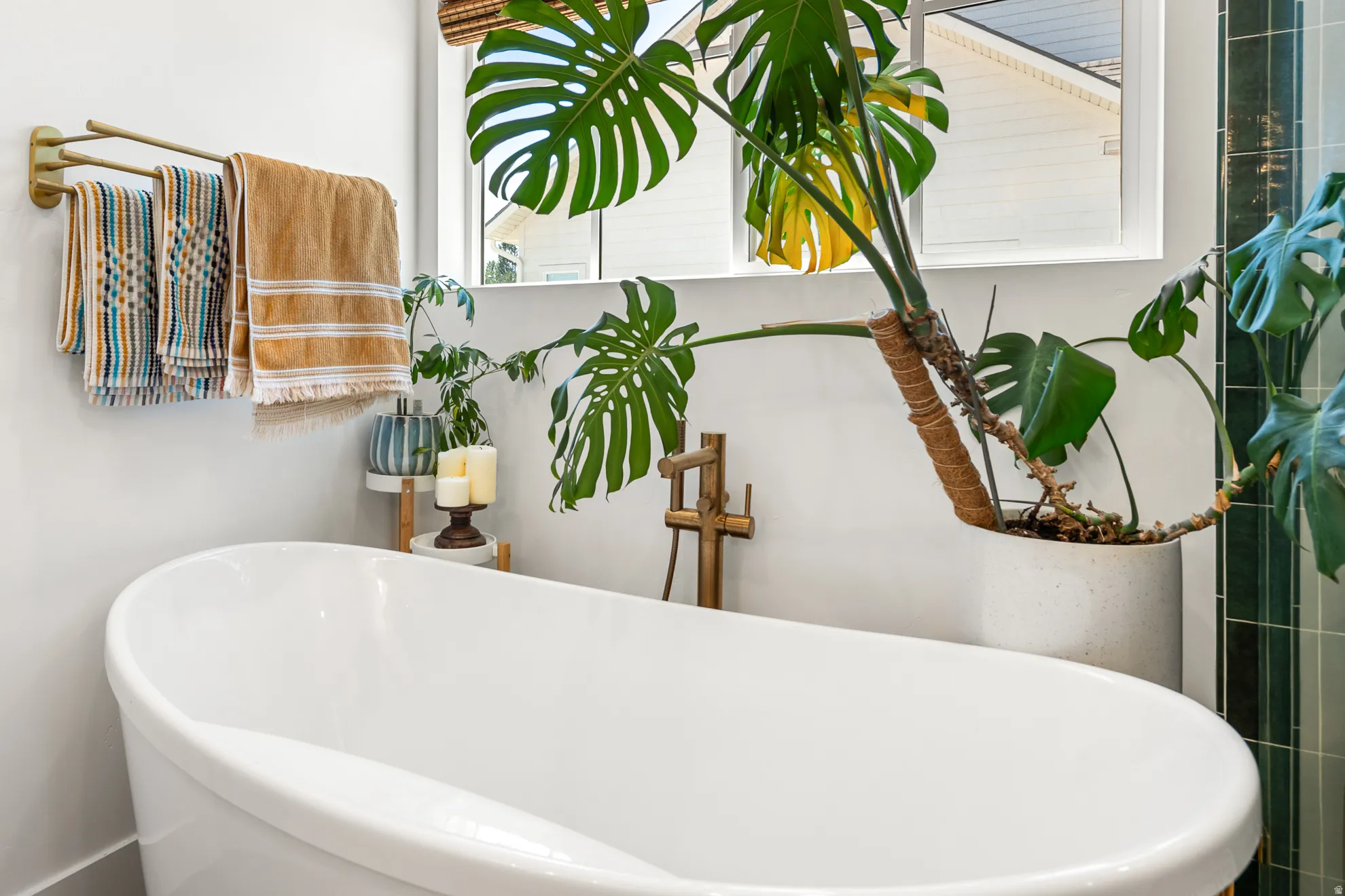 Freestanding soaking tub with a large window, a brass towel rack, and an adjacent tiled wall