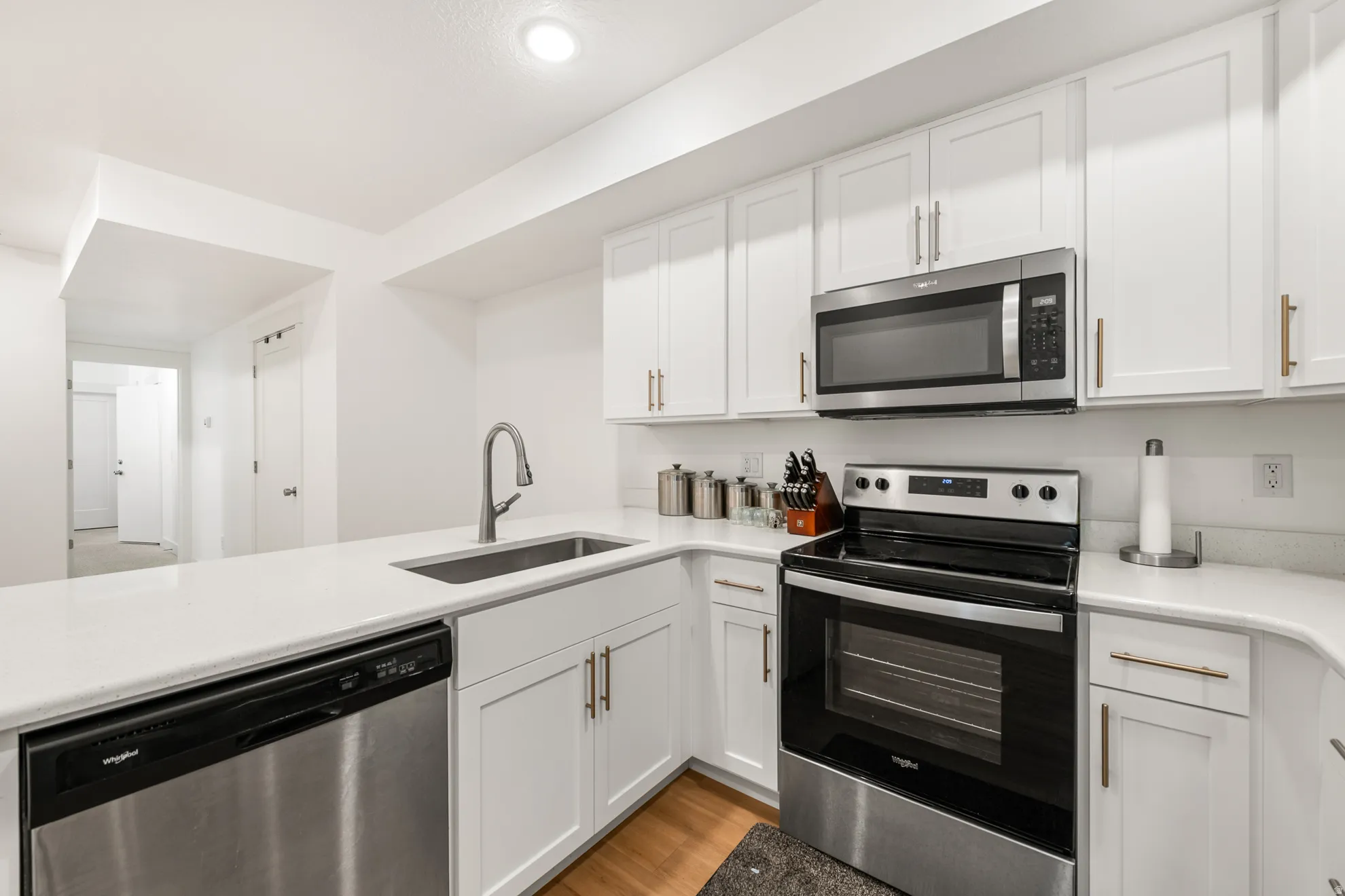 Kitchen featuring white shaker-style cabinetry, stainless steel appliances, a single-basin sink with a gooseneck faucet, light-toned countertops, and wood-finish flooring