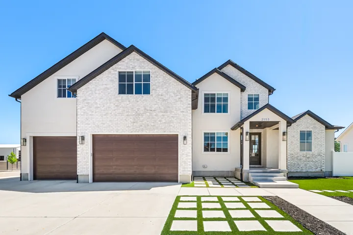 Contemporary two-story residence featuring a white brick and stucco exterior, dark trim, and a covered entryway