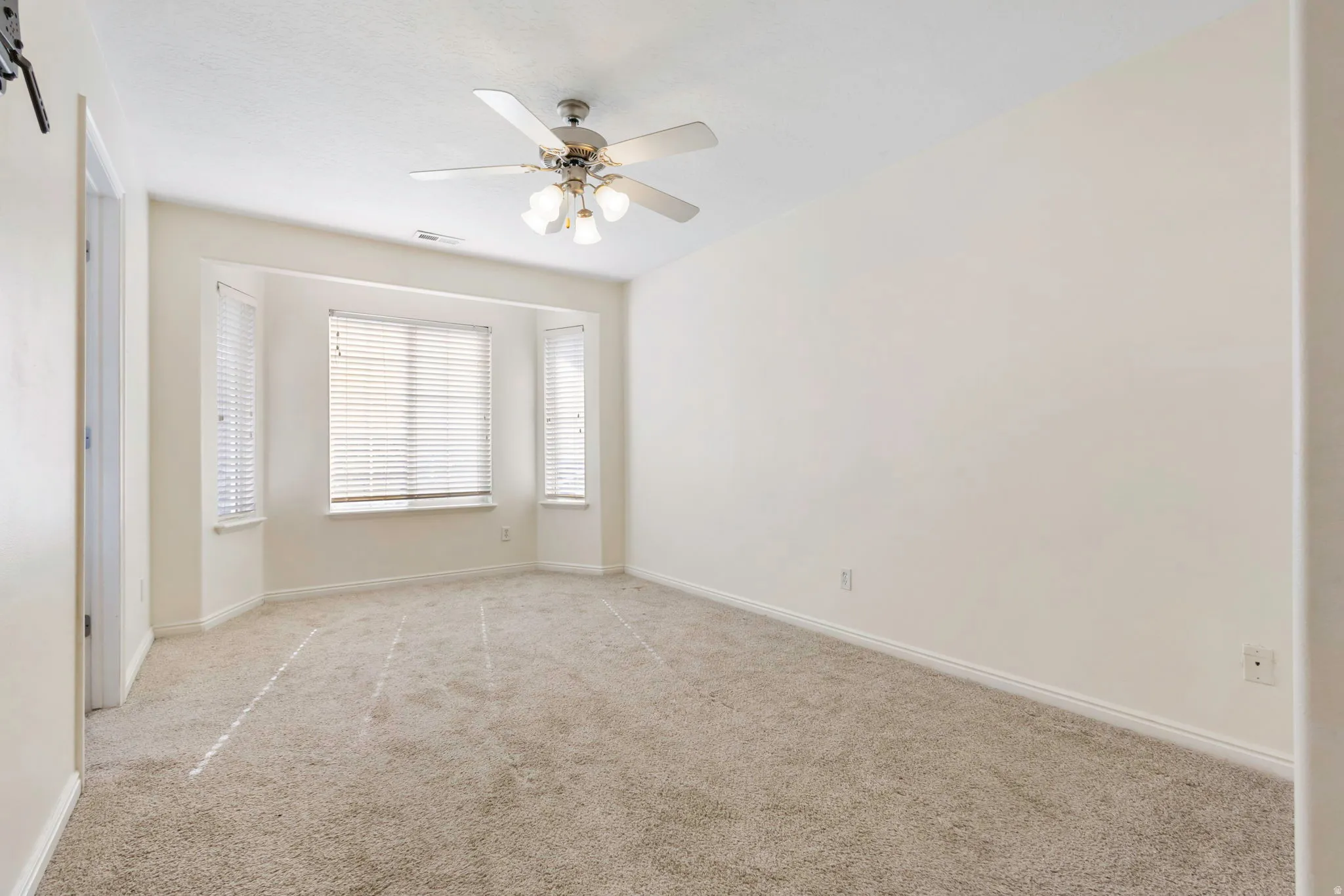 Carpeted room featuring a bay window with blinds, ceiling fan with integrated lighting, and white baseboards