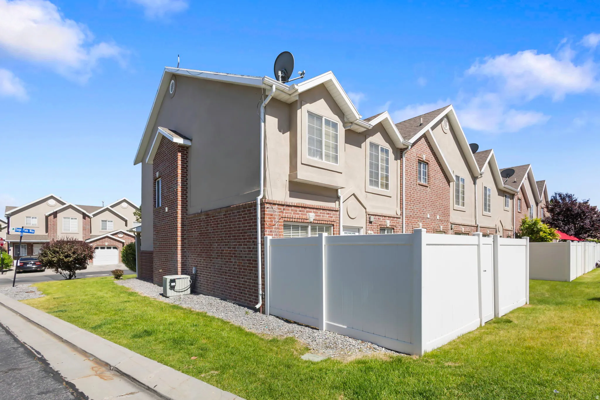 End-unit townhome with a brick and stucco exterior, featuring a white privacy fence and a manicured lawn
