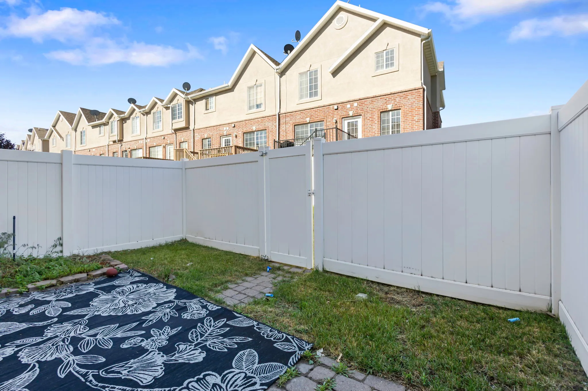 Enclosed backyard space featuring a private white vinyl fence, a paver patio area, and a grass section