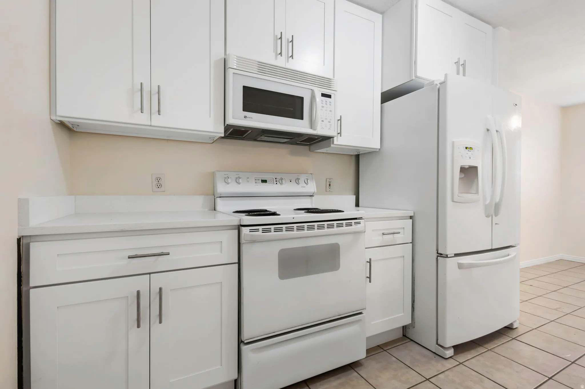 Kitchen featuring white cabinetry with silver-tone hardware, a white microwave, and a white refrigerator with a bottom freezer drawer