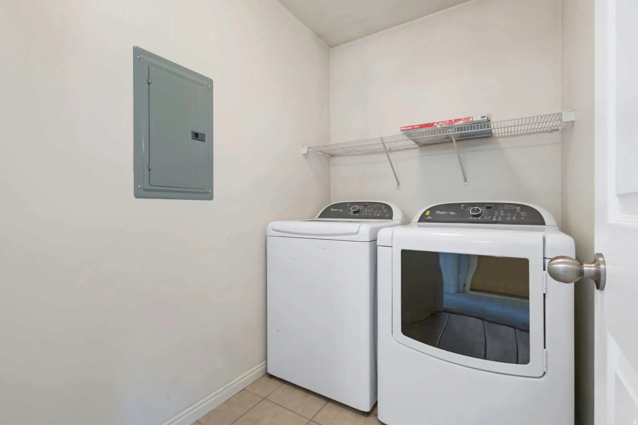 Dedicated laundry area featuring a washer and dryer, tiled flooring, and a wall-mounted wire shelf for storage