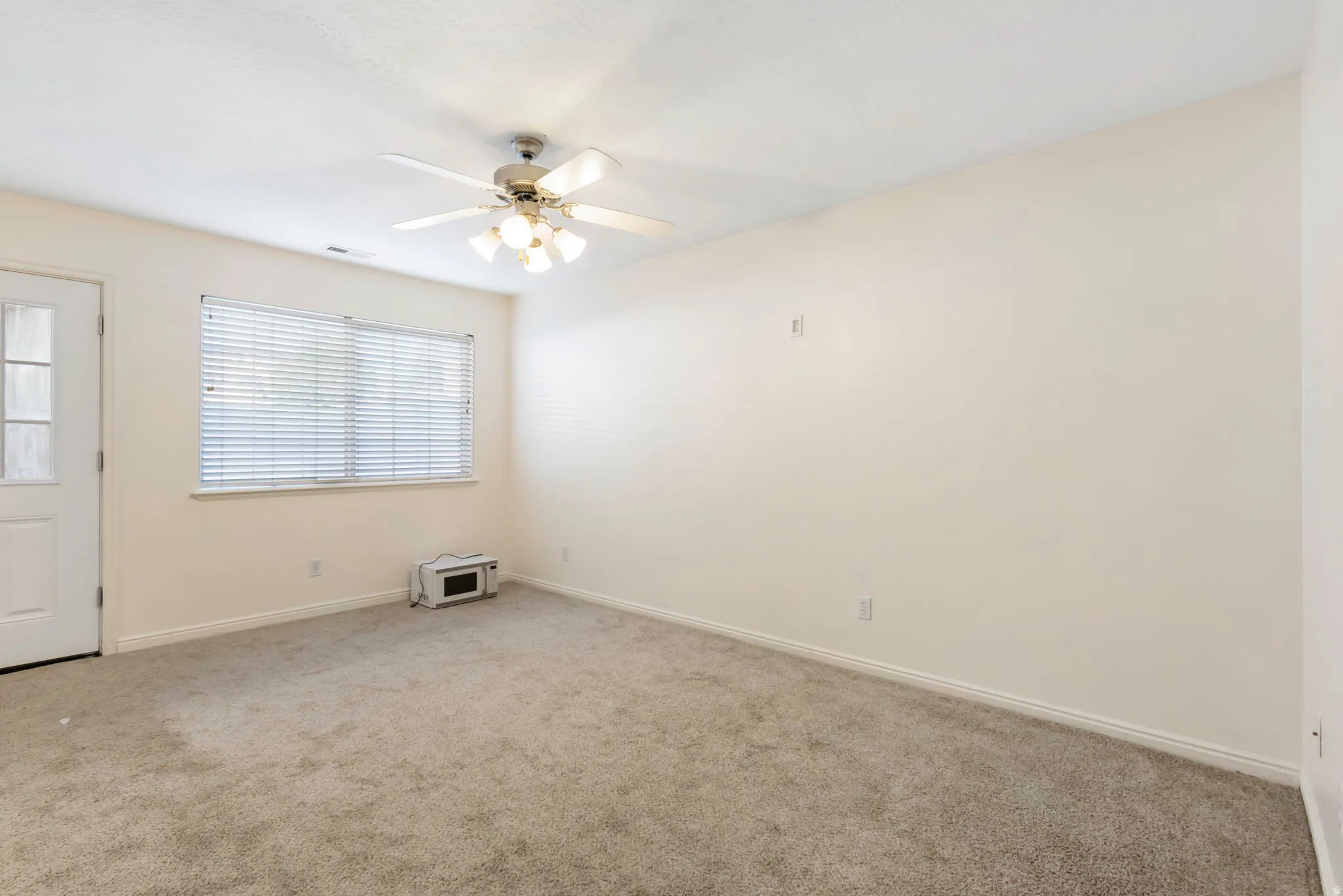 Carpeted room featuring a ceiling fan with integrated lighting, white walls, and a window with blinds