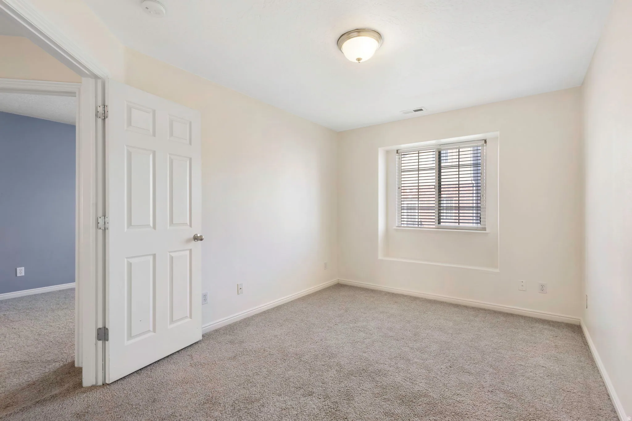 Carpeted room featuring a window with horizontal blinds, a flush-mount ceiling light, and light-colored walls