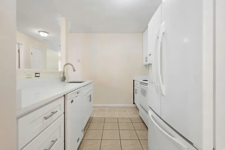 Kitchen with white cabinetry, stainless steel sink with gooseneck faucet, white appliances, and tiled flooring