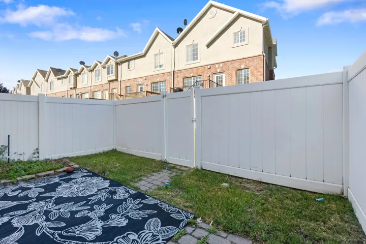Enclosed backyard space featuring a private white vinyl fence, a paver patio area, and a grass section