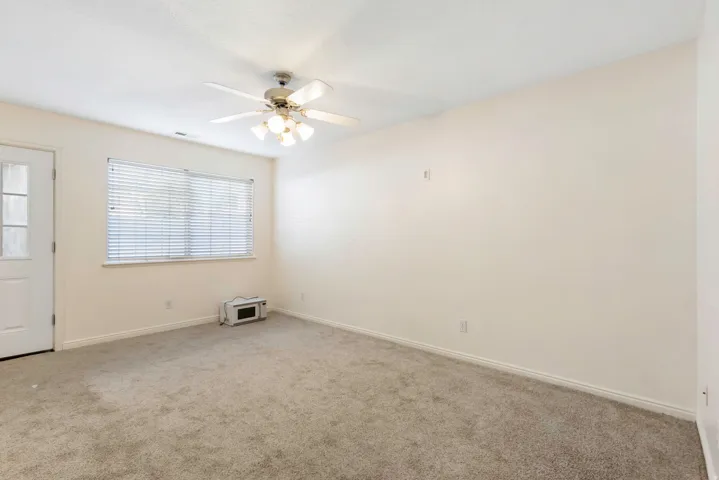 Carpeted room featuring a ceiling fan with integrated lighting, white walls, and a window with blinds