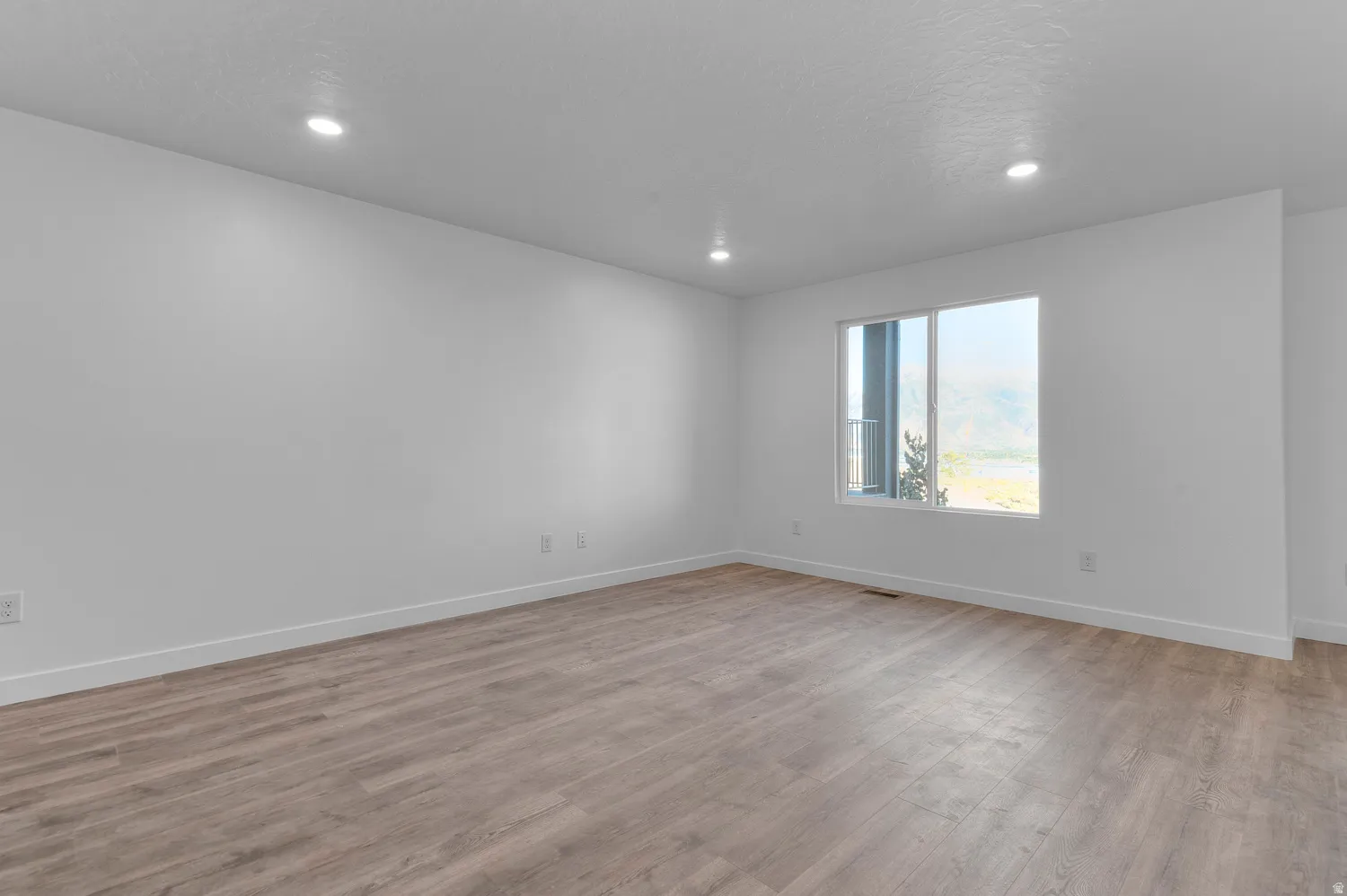 Spacious room featuring wood-finish flooring, recessed lighting, white walls, and a large window