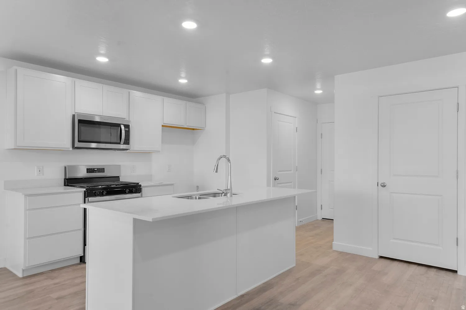 Modern kitchen featuring white cabinetry, stainless steel appliances, a center island with sink, and wood-finish flooring