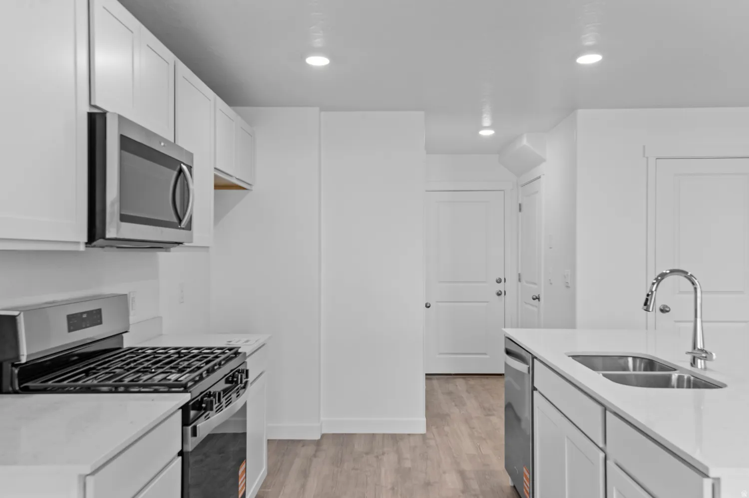 Modern kitchen featuring white shaker cabinetry, stainless steel appliances, a gas range, and wood-finish flooring