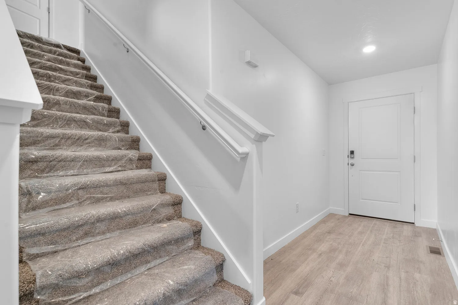 Entryway featuring wood-finish flooring, a white paneled door, and a staircase with carpeted treads