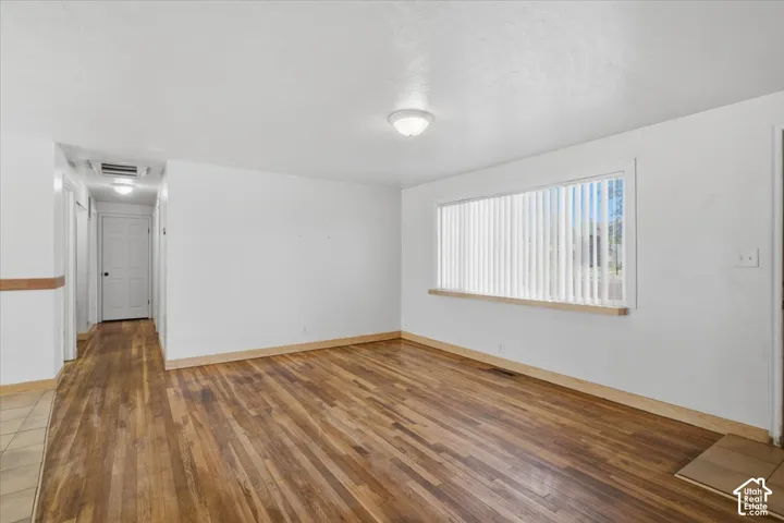 Hardwood flooring throughout, white painted walls, natural light from a window with vertical blinds, and a hallway with a white door