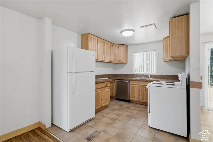 Kitchen featuring wood-finish cabinetry, stone-finish countertops, stainless steel dishwasher, and tiled flooring