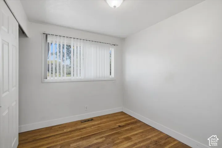 Wood-finish flooring, white walls, window with vertical blinds, and a built-in closet with bifold doors