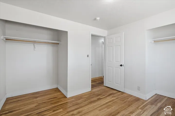 Wood-finish flooring with white baseboards, white painted walls, and built-in closet storage with hanging rods