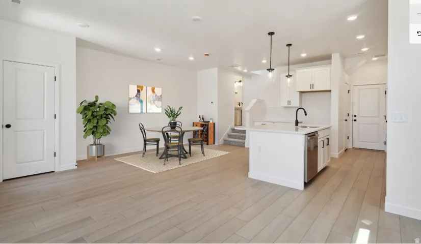 Spacious open-concept living area featuring light wood-finish flooring, recessed lighting, and a modern kitchen island with pendant lighting