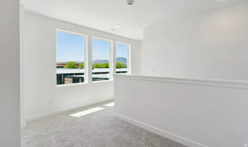 Upper level landing with three large windows, white walls, light gray carpet, and recessed lighting