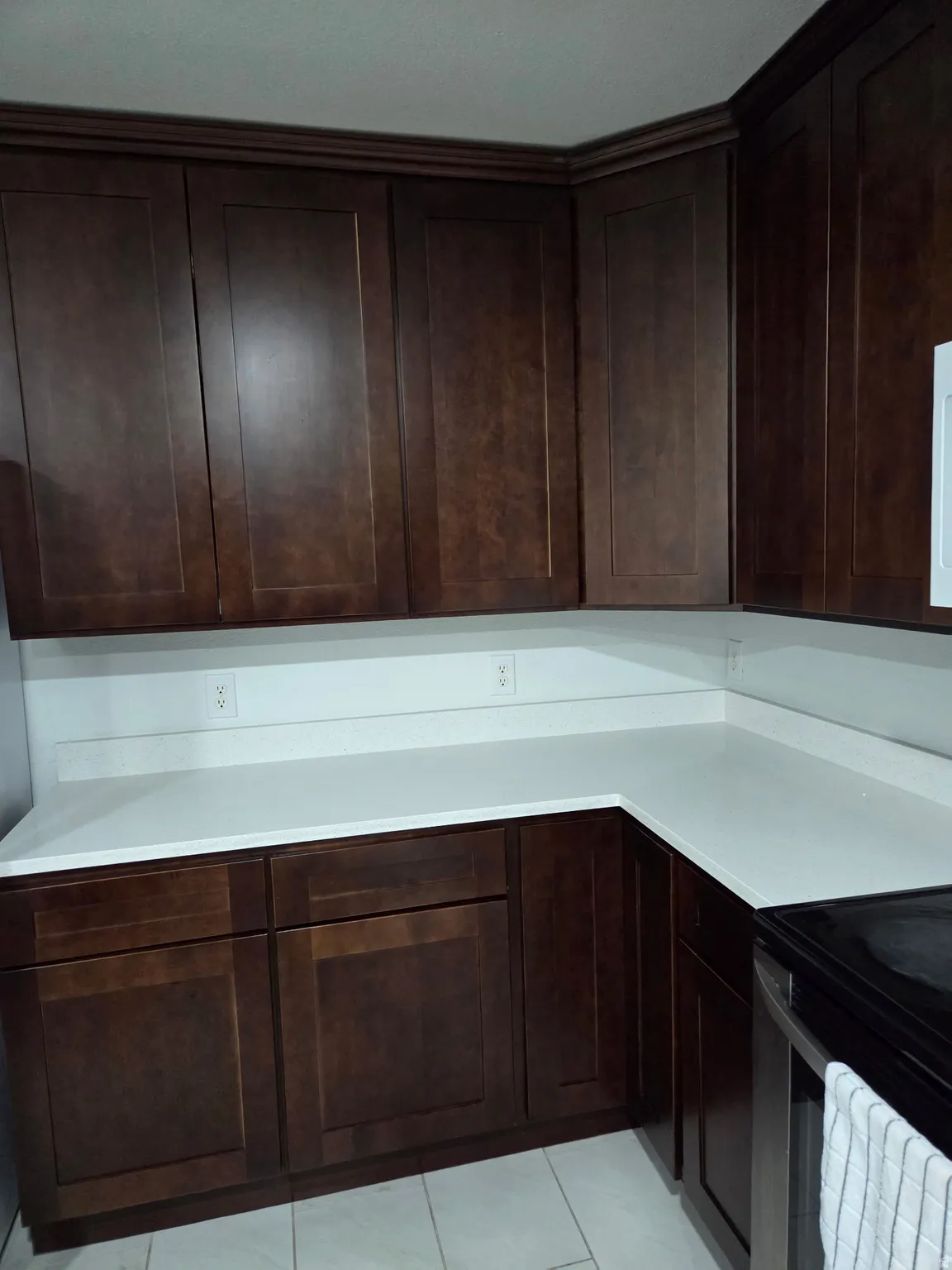 Kitchen featuring dark wood cabinetry with crown molding, white countertops, and a white tile flooring