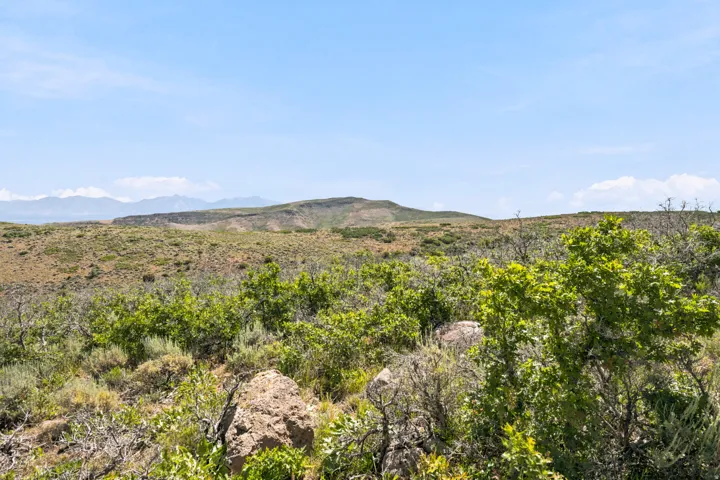 Expansive undeveloped land featuring natural rock formations, varied scrub brush, and distant mountain ranges under a clear sky