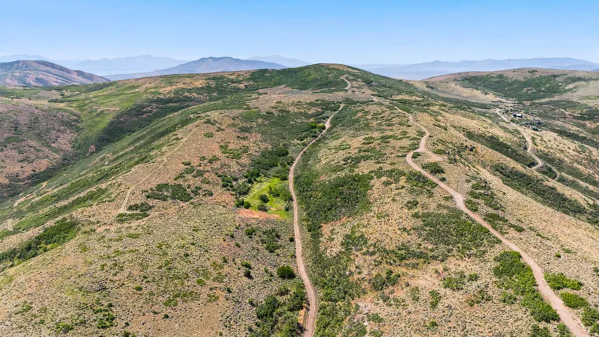 Expansive mountainous terrain featuring winding dirt paths and scattered green foliage