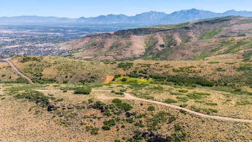 Expansive mountain landscape featuring varied terrain, a distant city horizon, and a distinct mountain range backdrop