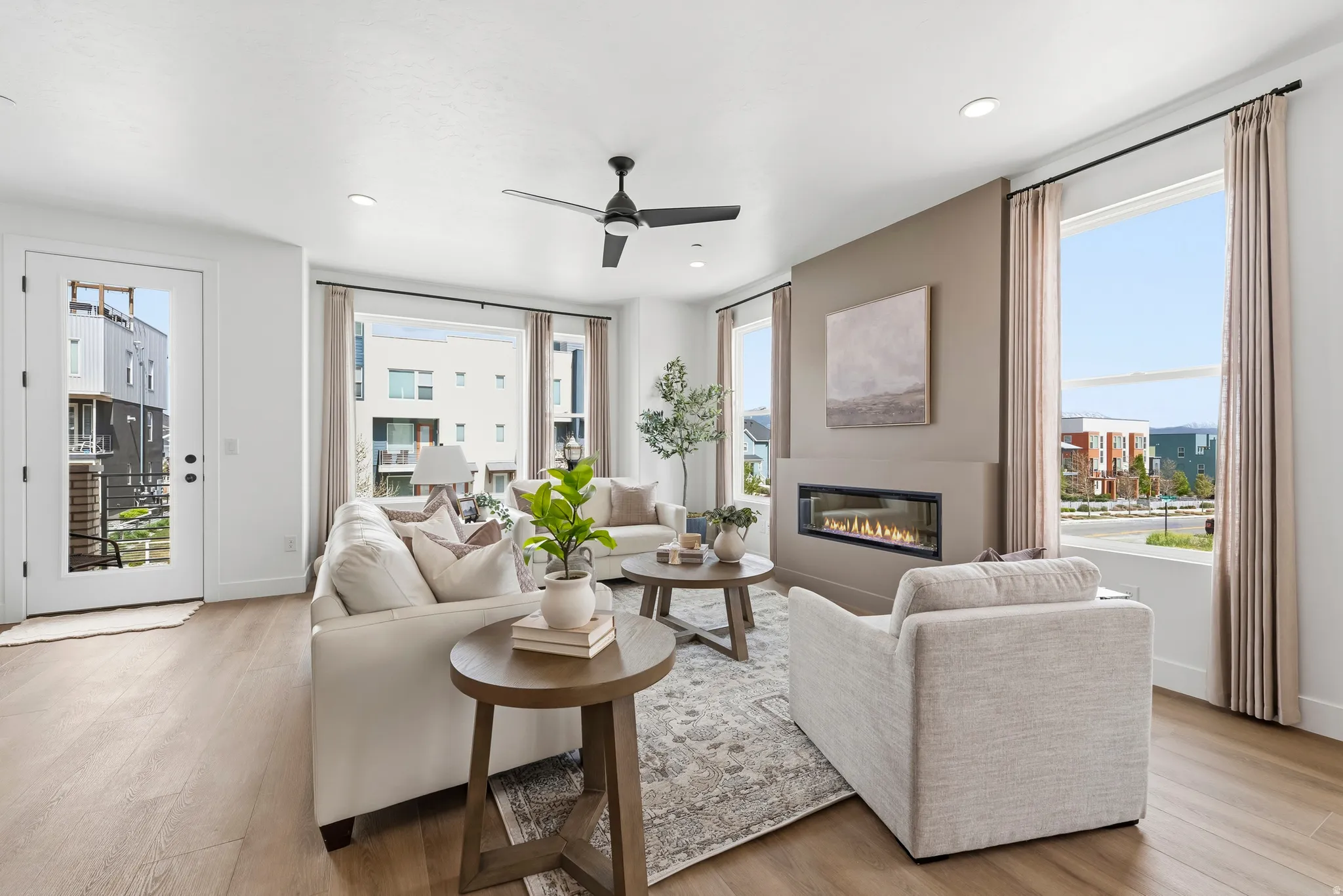 Open-concept living space with light wood-finish flooring, a contemporary linear fireplace, and expansive windows