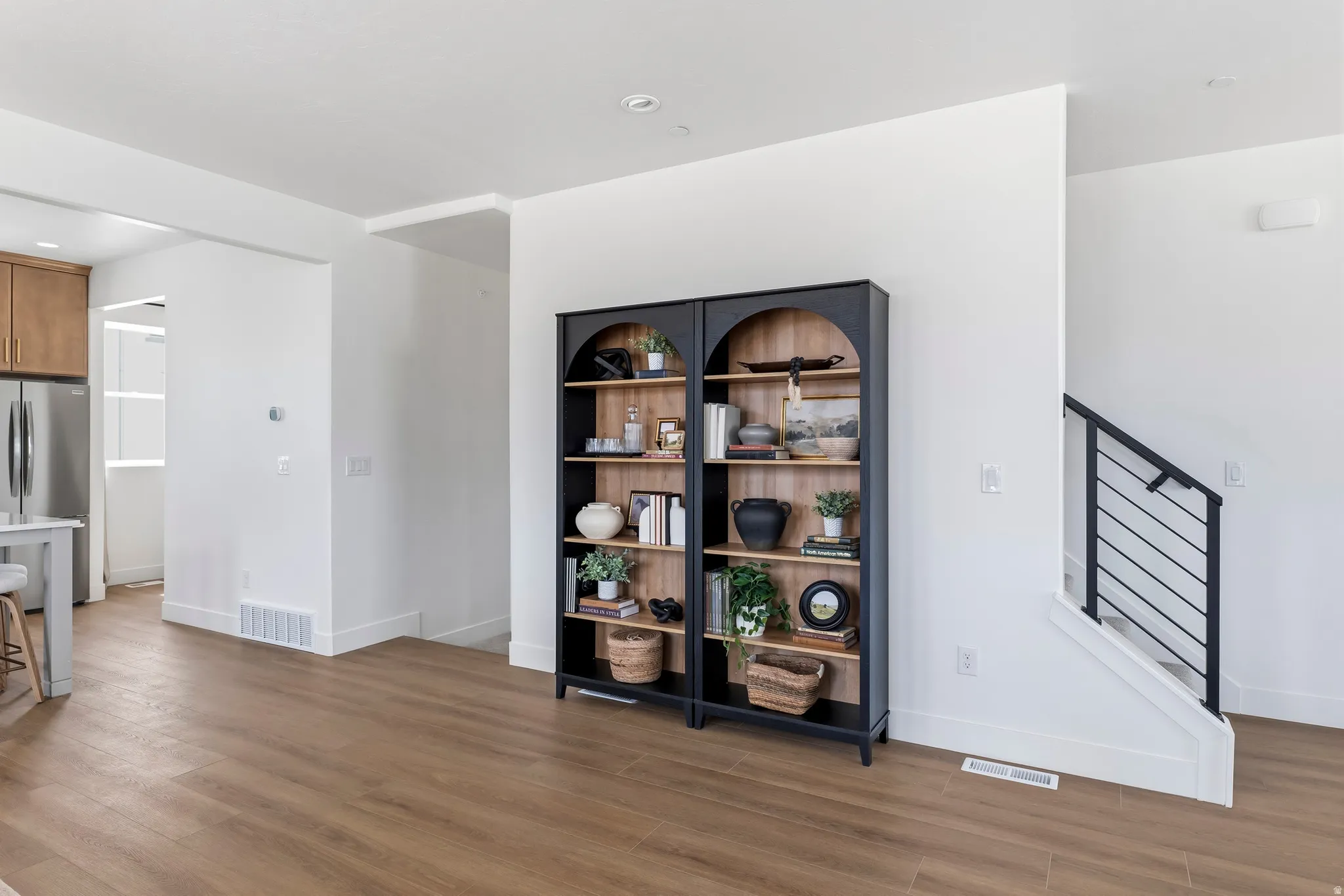 Open-concept interior featuring wood-finish flooring, white walls, and a contemporary staircase with black metal railings
