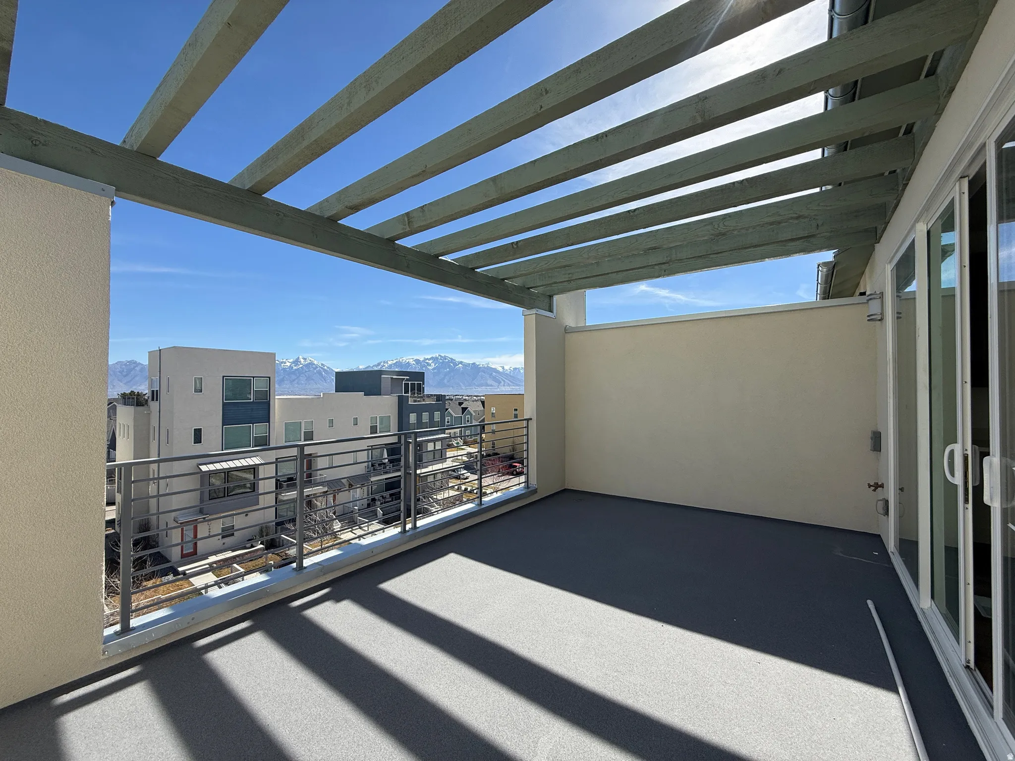 Spacious outdoor patio featuring a slatted pergola, textured flooring, and a metal railing