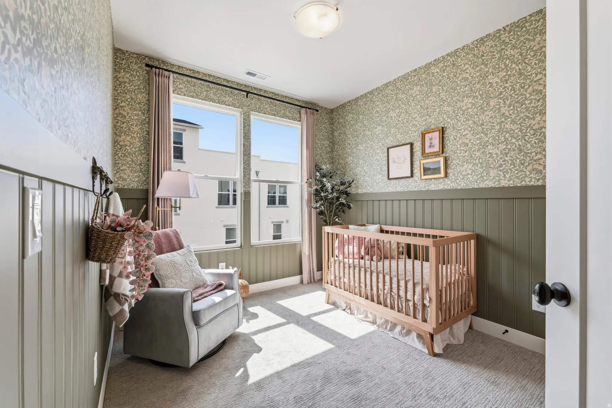 Room featuring two large windows with full privacy drapes, decorative patterned wallpaper, painted wainscoting, and carpet flooring