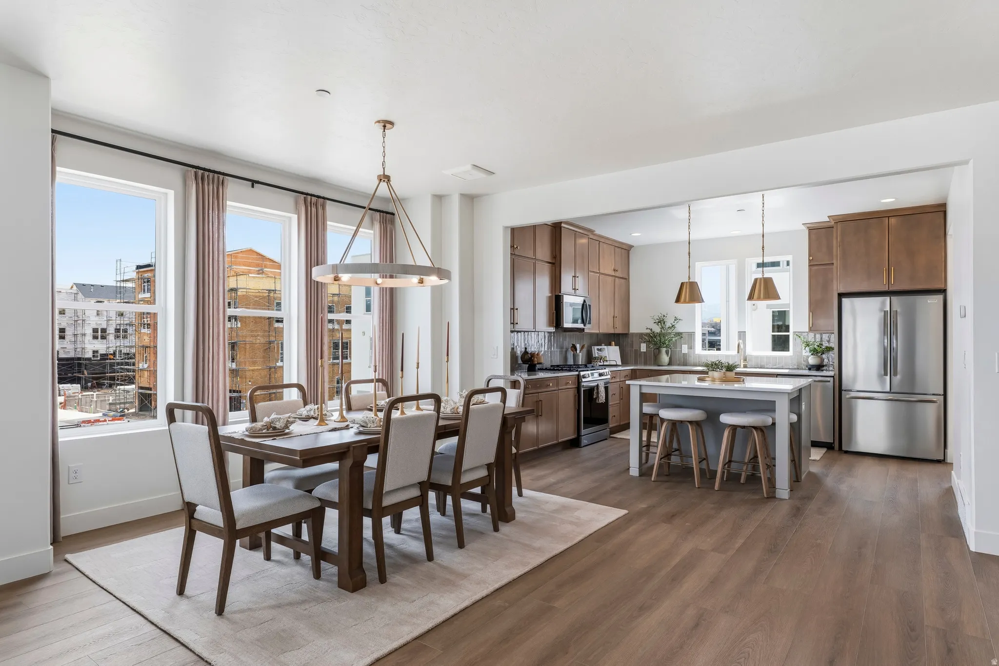 Open-concept living space with wood-finish flooring, a contemporary kitchen, stainless steel appliances, a center island with seating, and a formal dining area