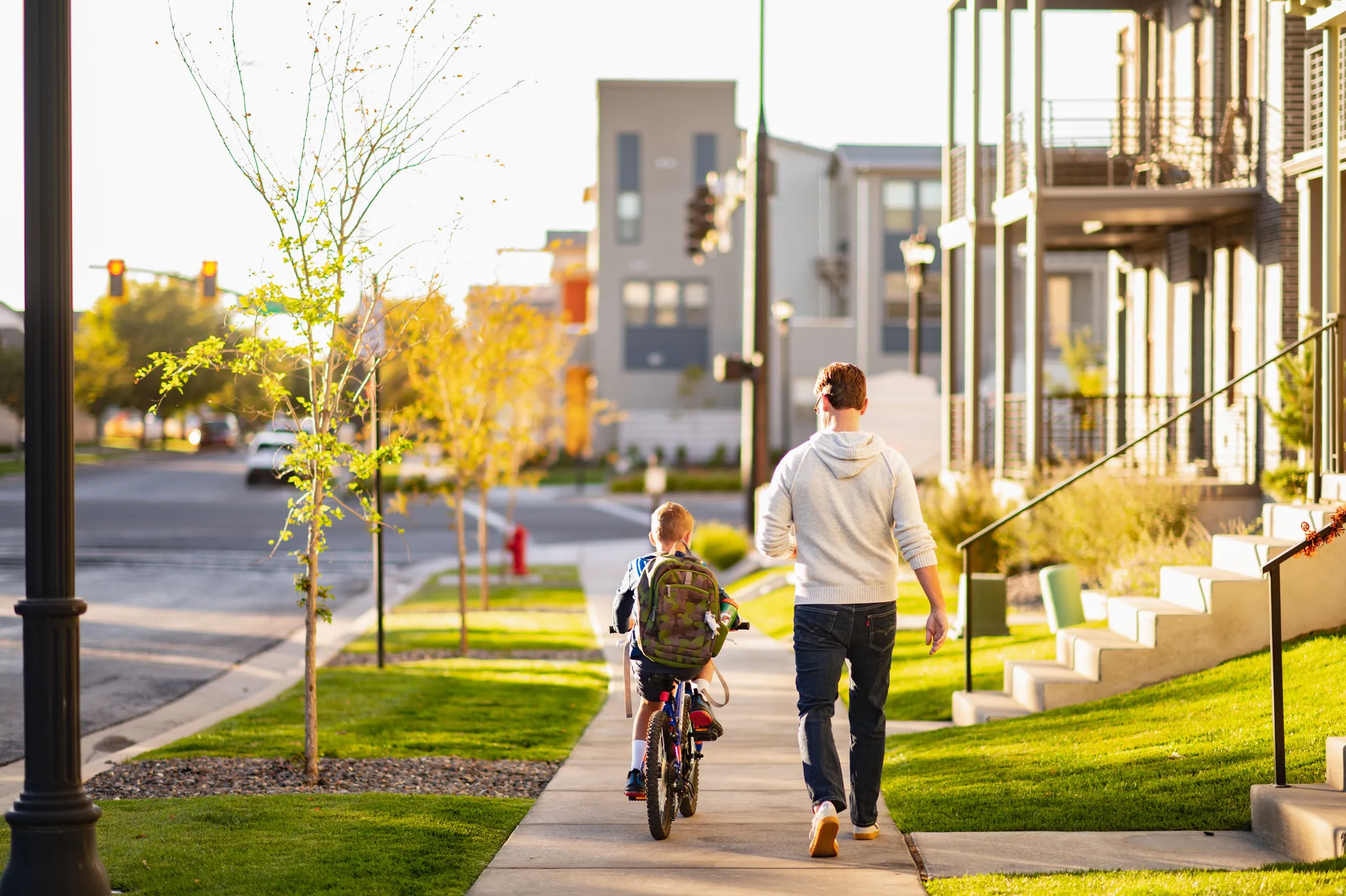 Sidewalk streetscape featuring manicured lawns, young trees, and modern townhome-style residences with balconies and exterior staircases