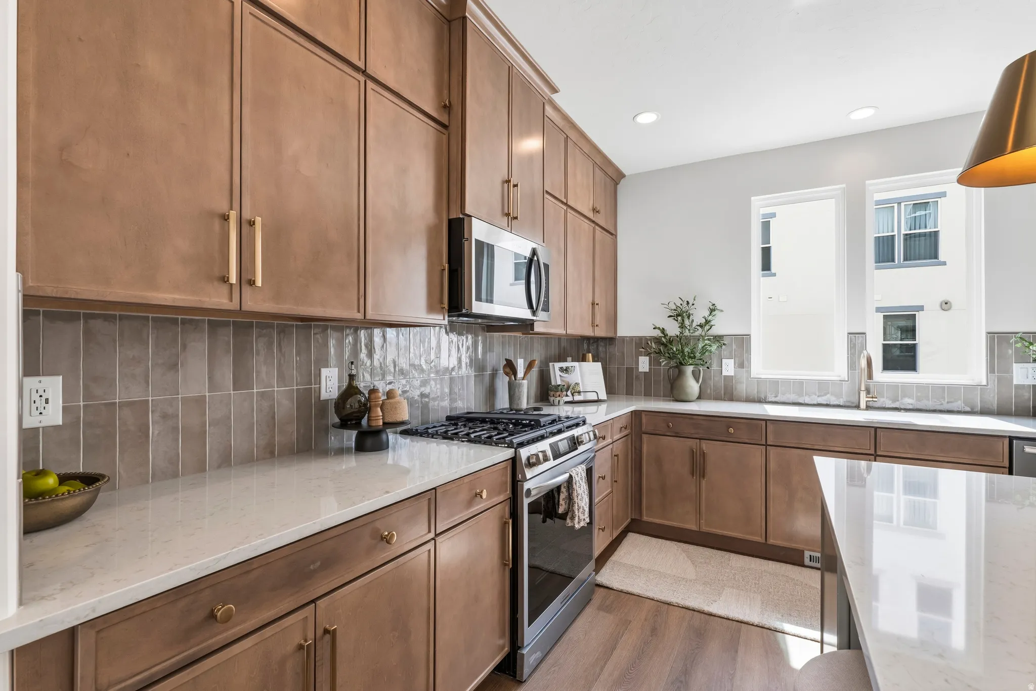 Kitchen featuring extensive wood-finish cabinetry, light-toned countertops, a stainless steel gas range, and a tiled backsplash