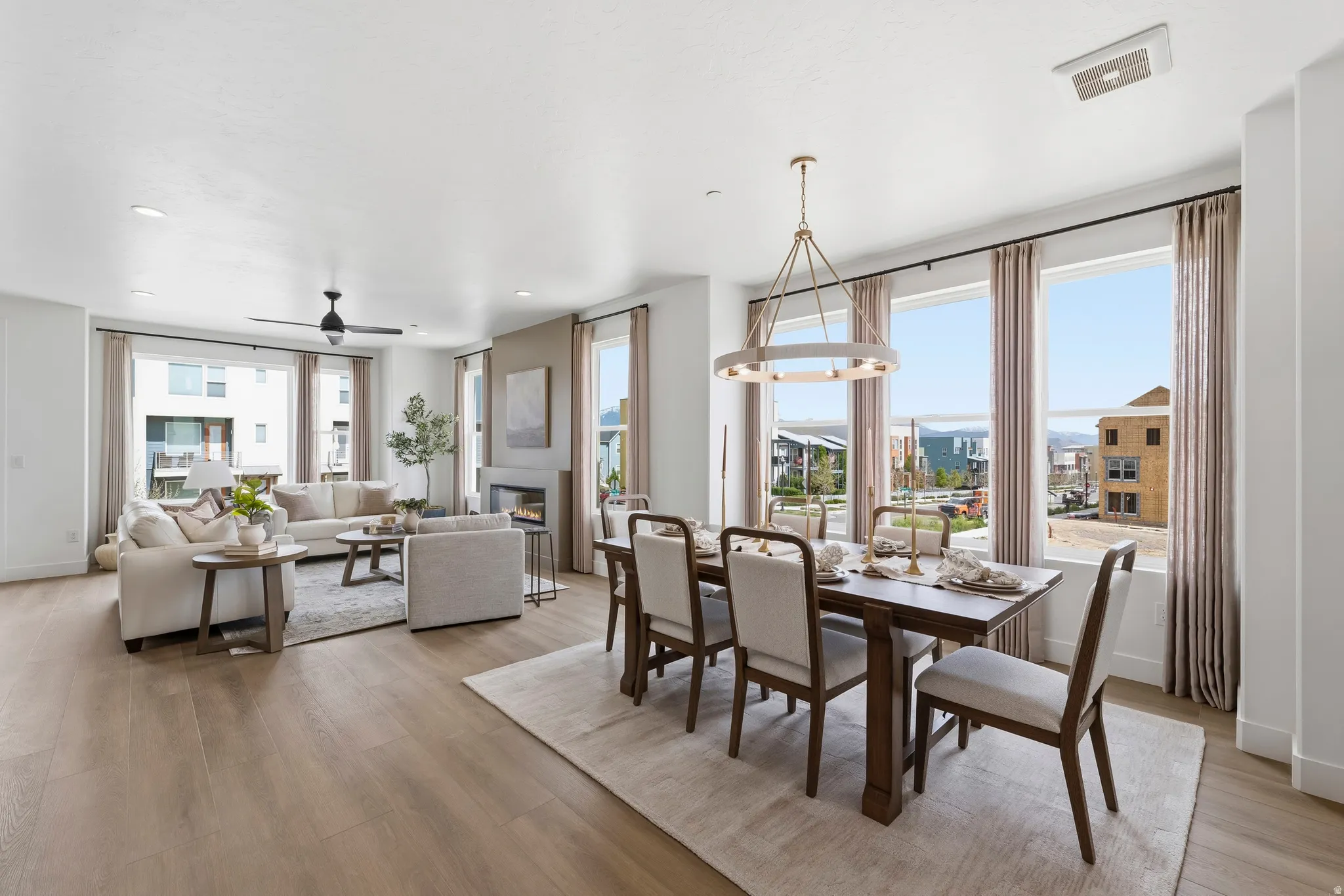 Open-concept living and dining area featuring wood-finish flooring, a contemporary chandelier, a built-in fireplace with a stone-finish surround, and multiple large windows