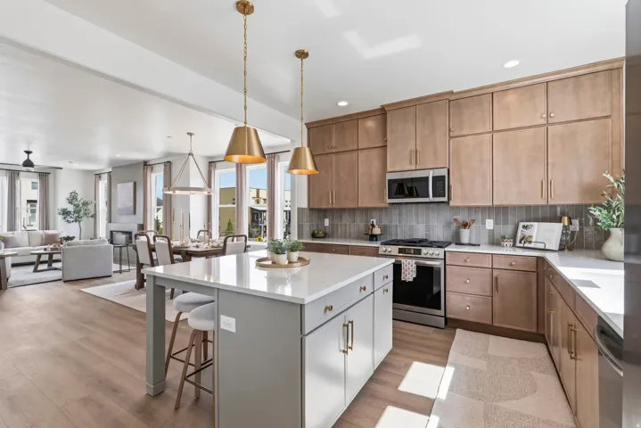Modern kitchen featuring a central island with white quartz countertops, stainless steel appliances, light wood-finish cabinetry, and a gray subway tile backsplash