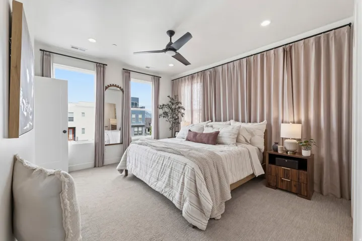 Bedroom featuring light-toned carpeting, dual windows with ample natural light, and a ceiling fan with integrated lighting