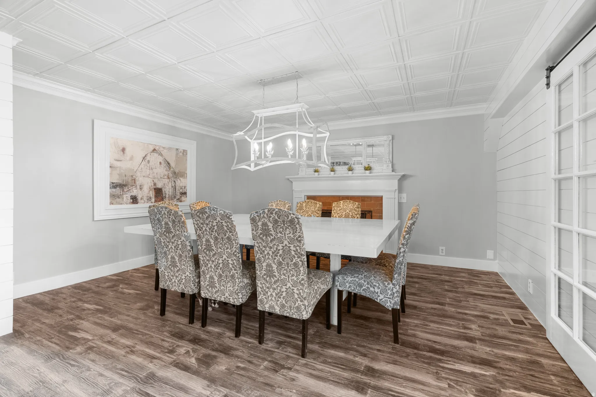 Spacious formal dining area featuring LPV  flooring, a white coffered ceiling, a decorative fireplace with mantel, and a sliding barn door with glass panels