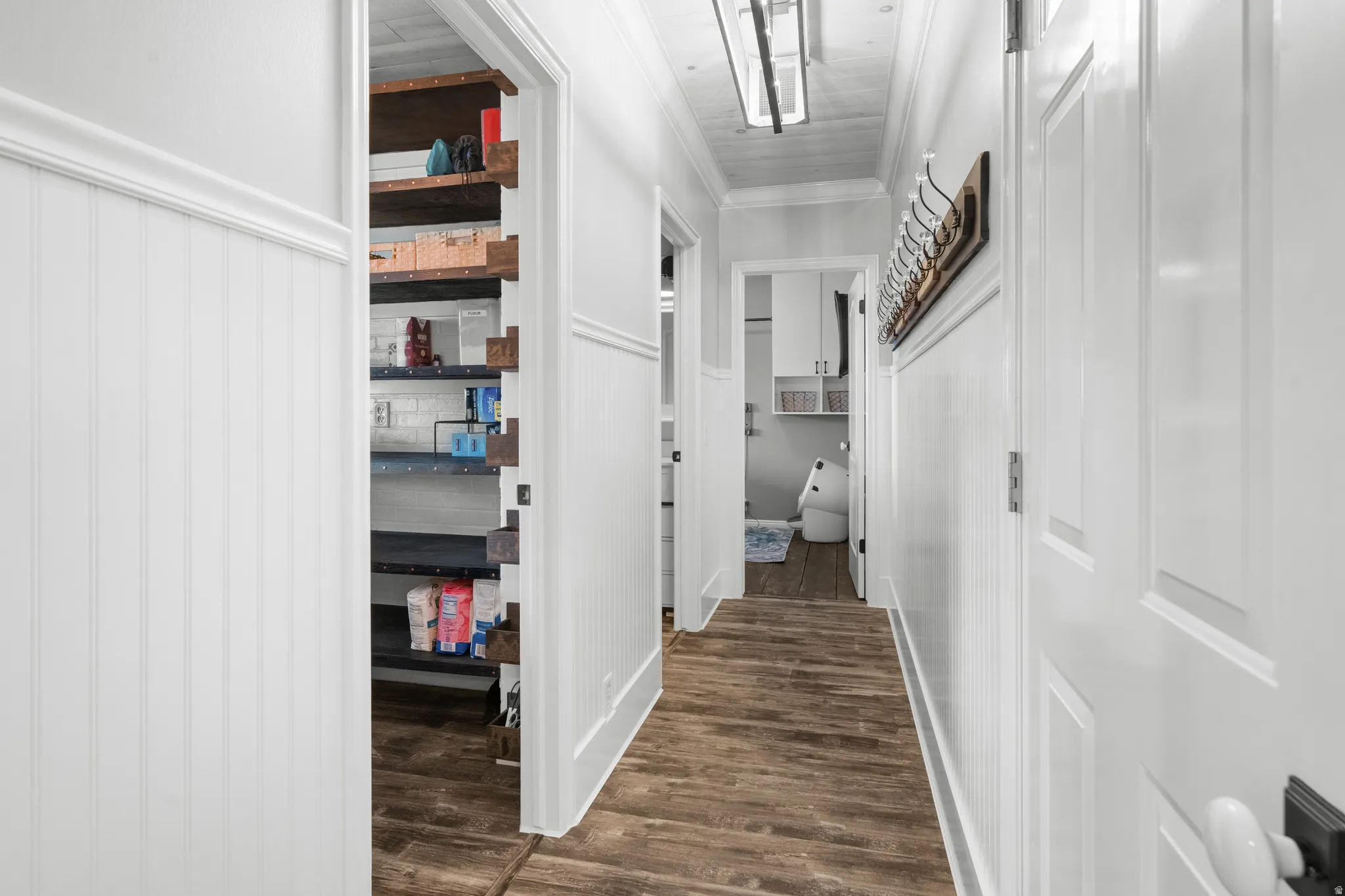 Hardwood-style flooring throughout a hallway featuring white wainscoting and crown molding