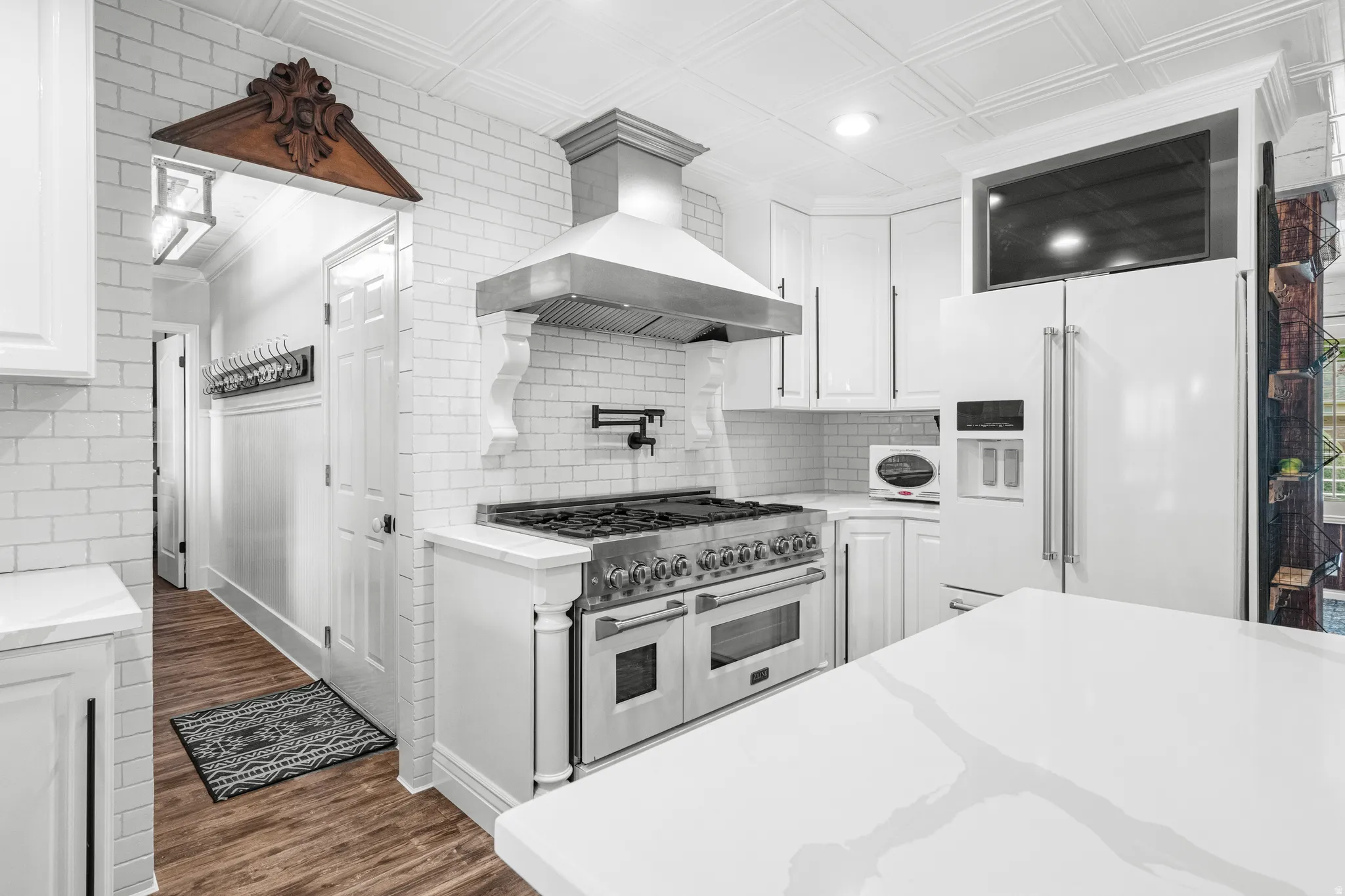 Gourmet kitchen featuring a professional-grade range, stainless steel vent hood, classic white subway tile backsplash, quartz countertops, and abundant storage, perfectly designed for both everyday living and entertaining.