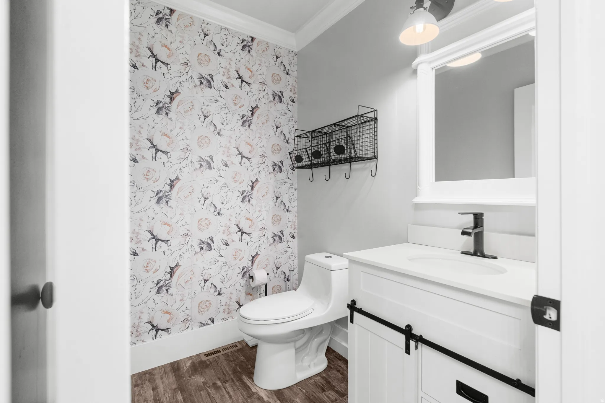 Half bath room featuring botanical print wallpaper, LVP flooring, white vanity with, matte black faucet, and a wall-mounted mirror with integrated lighting