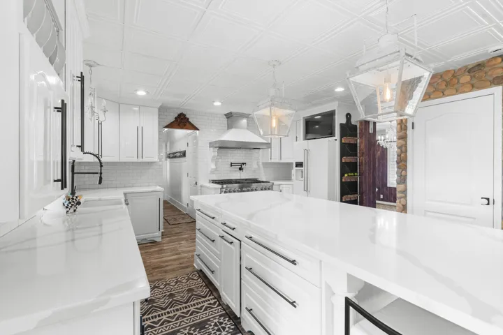 Spacious kitchen featuring white cabinetry, quartz countertops, LVP flooring, a decorative elegant ceiling, and pendant lighting