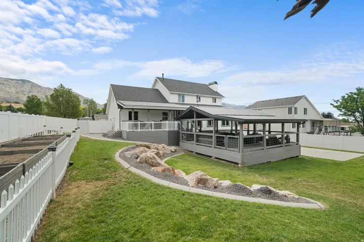 Spacious backyard featuring a covered patio, elevated deck with white railings, and a beautifully landscaped rock garden. The yard also includes eight fenced raised garden beds, providing ample space for gardening, flowers, or homegrown produce
