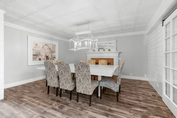 Spacious formal dining area featuring LPV  flooring, a white coffered ceiling, a decorative fireplace with mantel, and a sliding barn door with glass panels