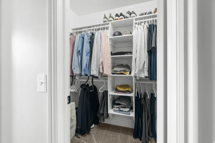 Primary dual walk-in closets featuring built-in shelving, multiple hanging rods, and neutral-toned carpeting