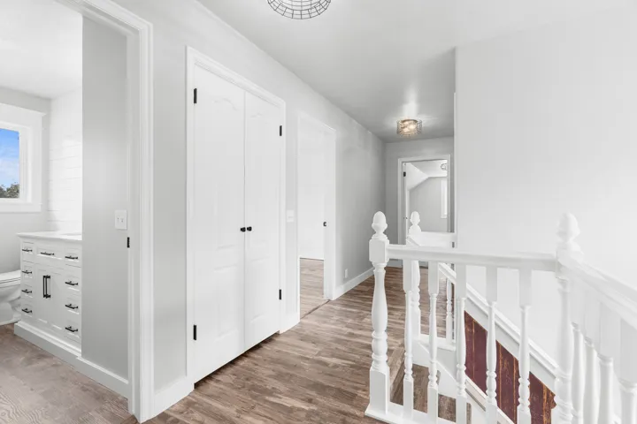 Upper-level hallway featuring custom LVP flooring, white paneled doors with black hardware, recessed ceiling lighting, and a white baluster staircase