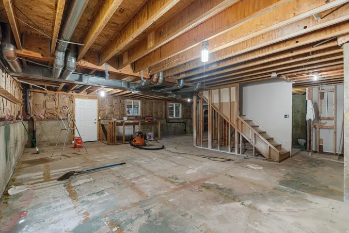 Unfinished basement space featuring exposed wooden ceiling joists, concrete flooring, partially framed walls, and an unfinished staircase