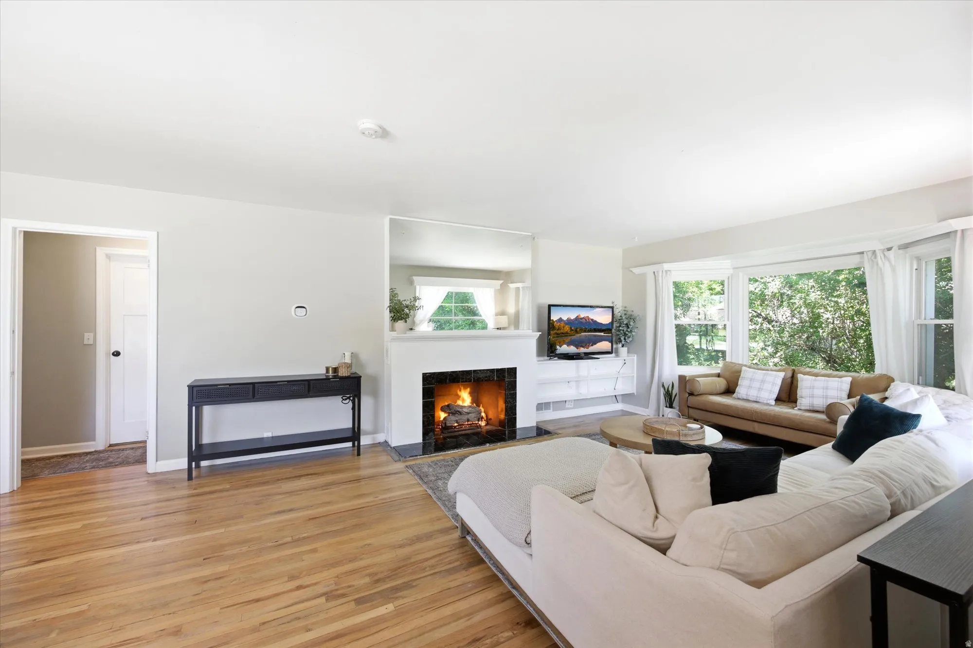 Living room featuring light wood-finish flooring, a white mantel fireplace with a dark hearth, and expansive windows