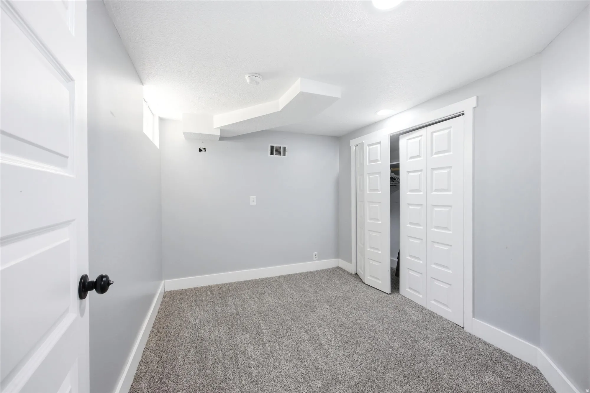 Carpeted room featuring light gray walls, white baseboards, and a white six-panel door with a black knob