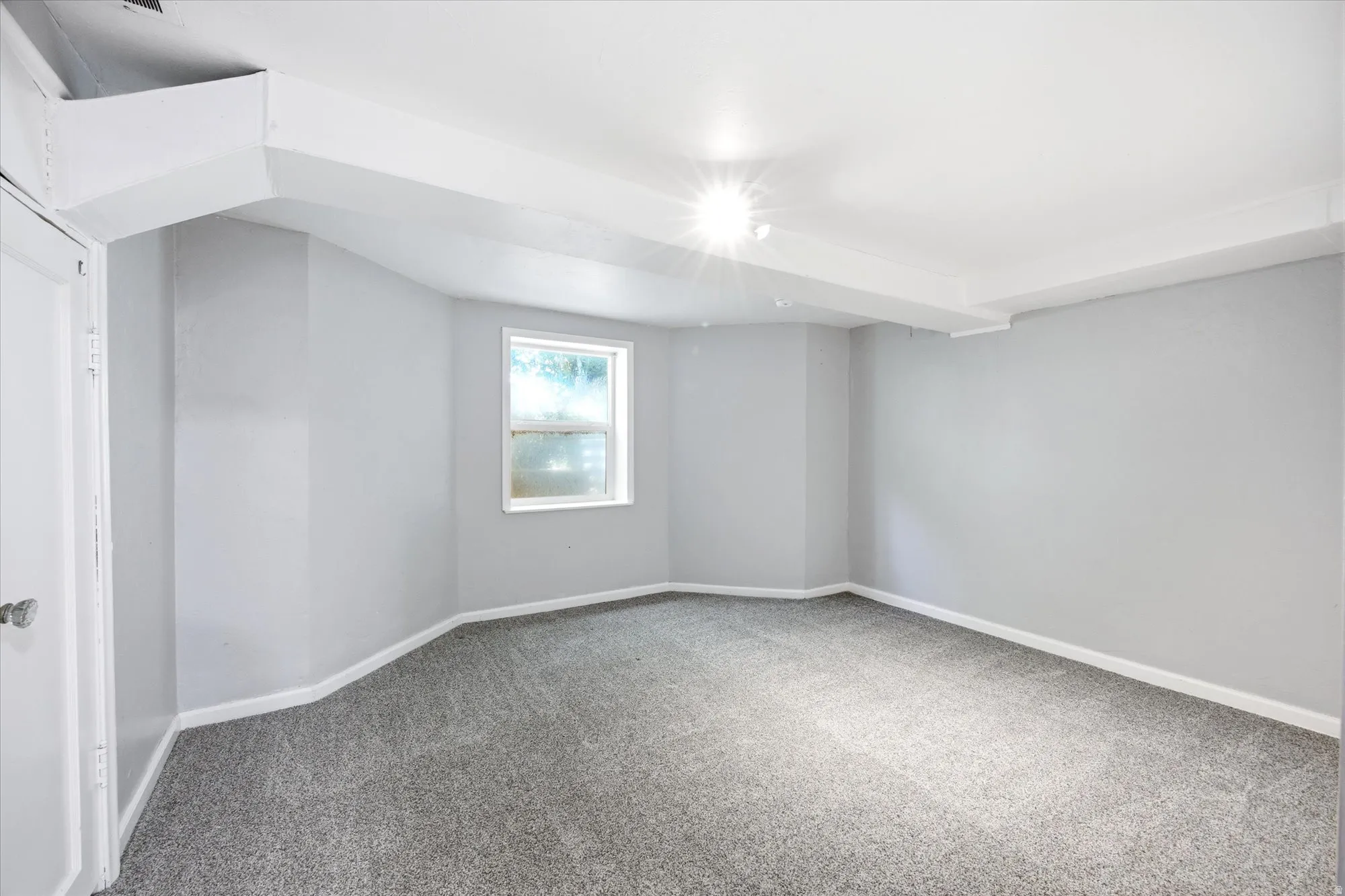 Room featuring light gray walls, gray carpet, a single window, white trim, and a white ceiling with exposed beams